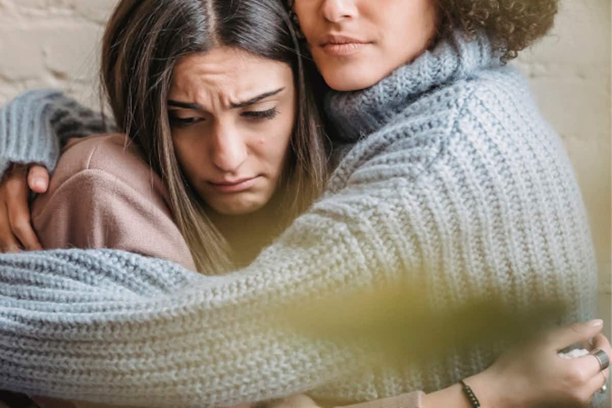 Image with two women hugging looking sad
